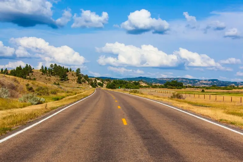 An empty two-lane Montana road under a big blue sky